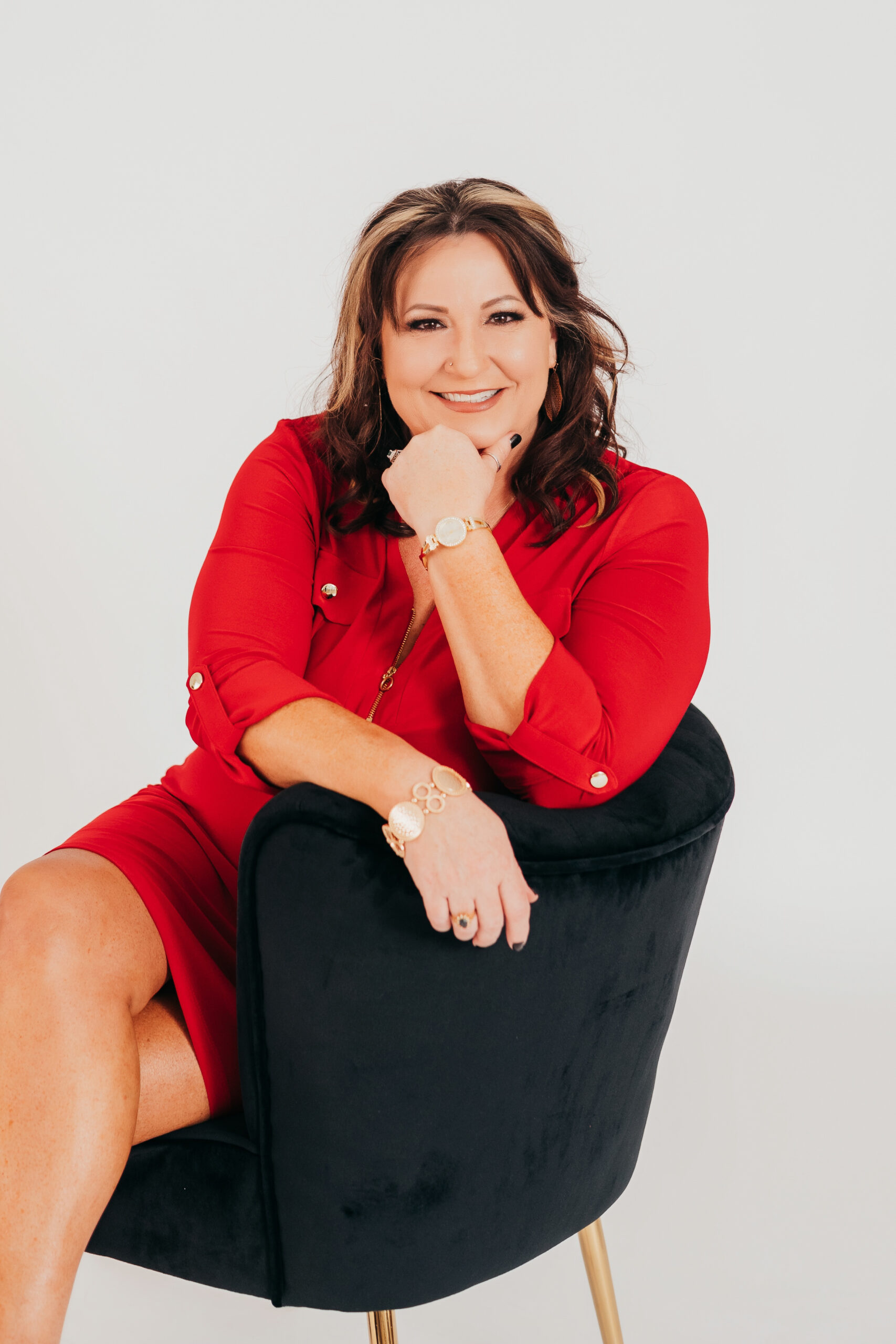 Portrait of the founder of Arpco Legacy Enterprises, smiling confidently while seated in a black chair, wearing a red dress — award-winning leadership consultant.