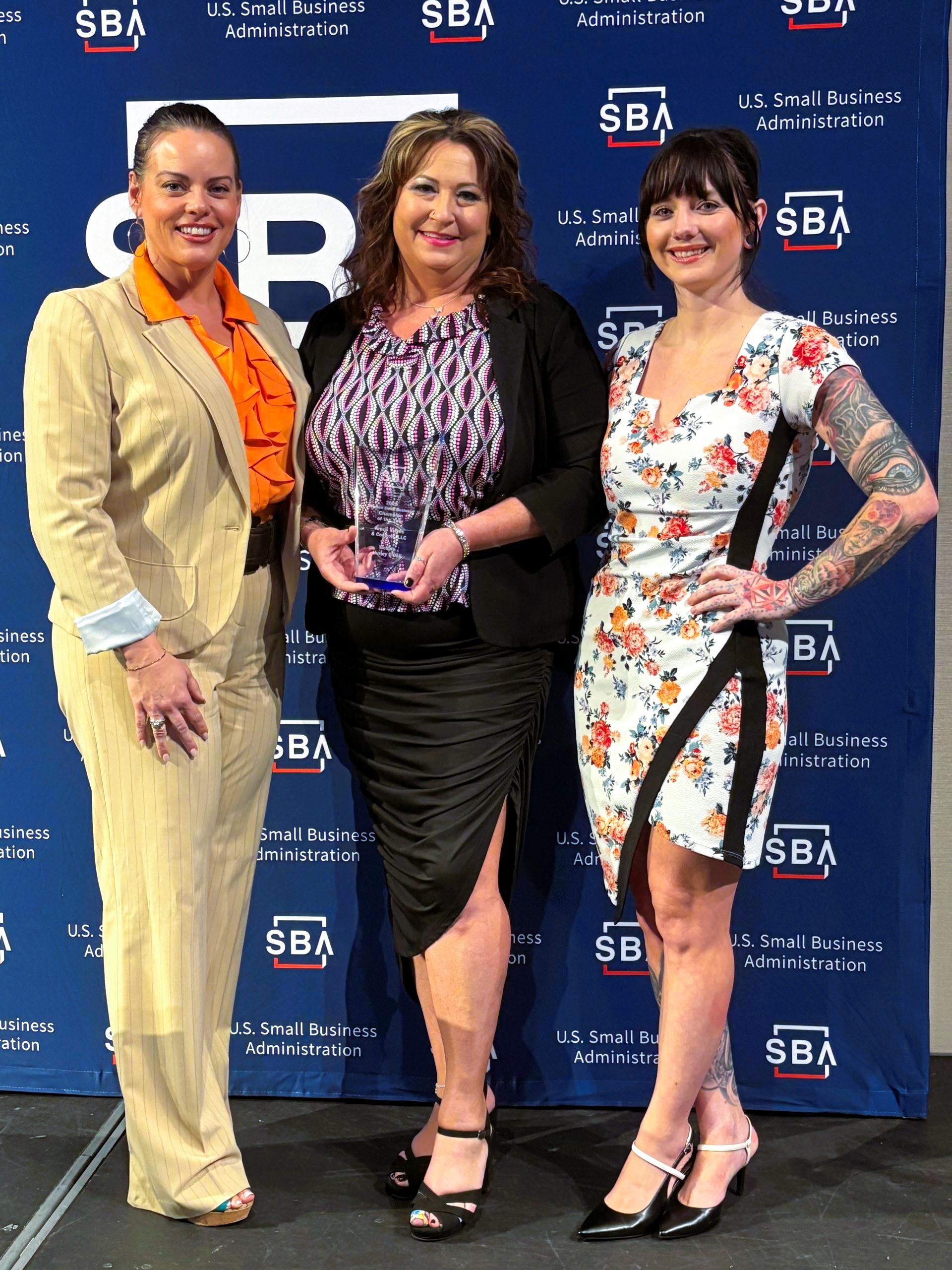 Bobbie Hurley center) receiving the 2025 SBA Woman-Owned Business Champion Award, standing with two colleagues in front of an SBA backdrop.