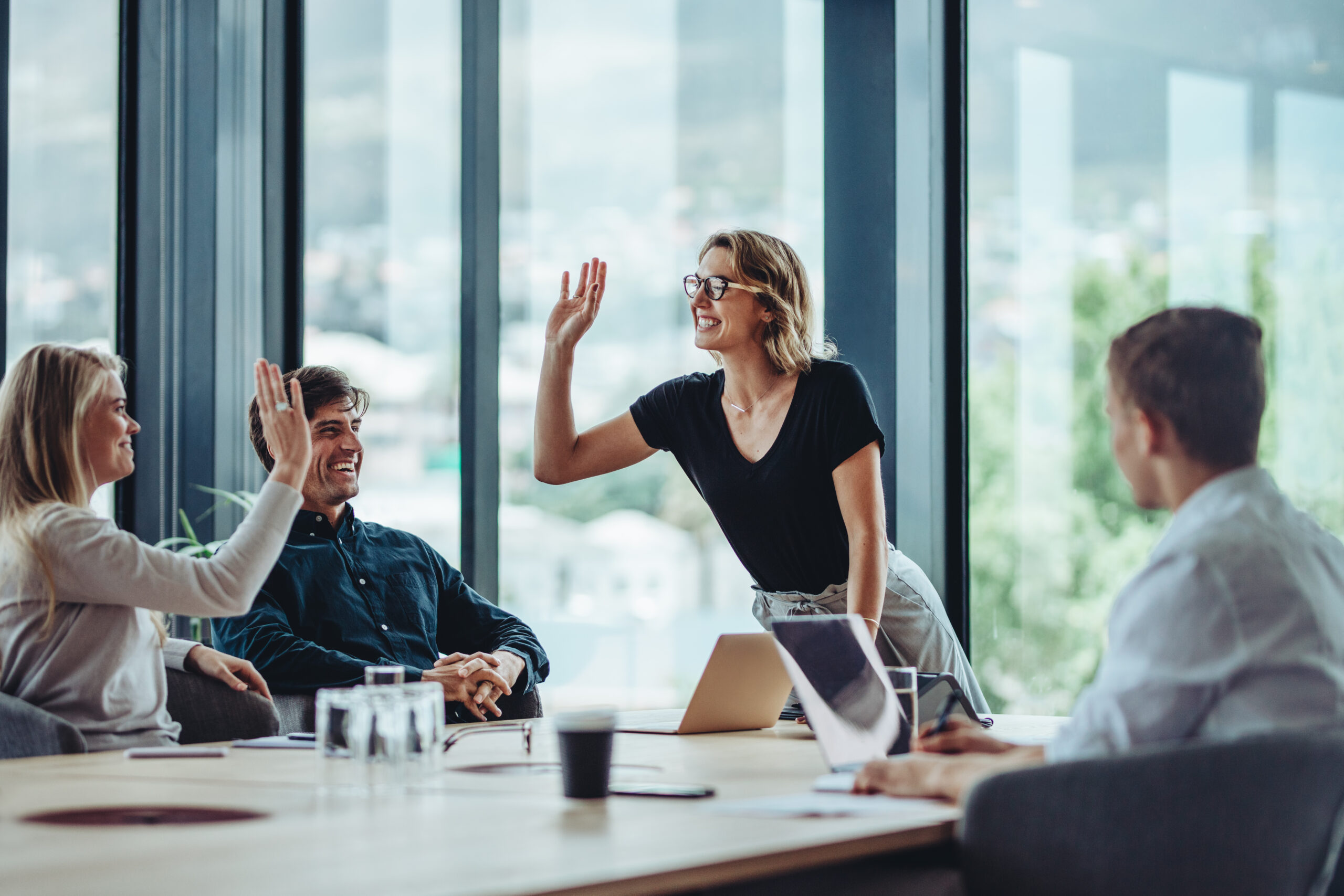 Business team celebrating success with a high five around a conference table – symbolizing leadership and aligned collaboration.