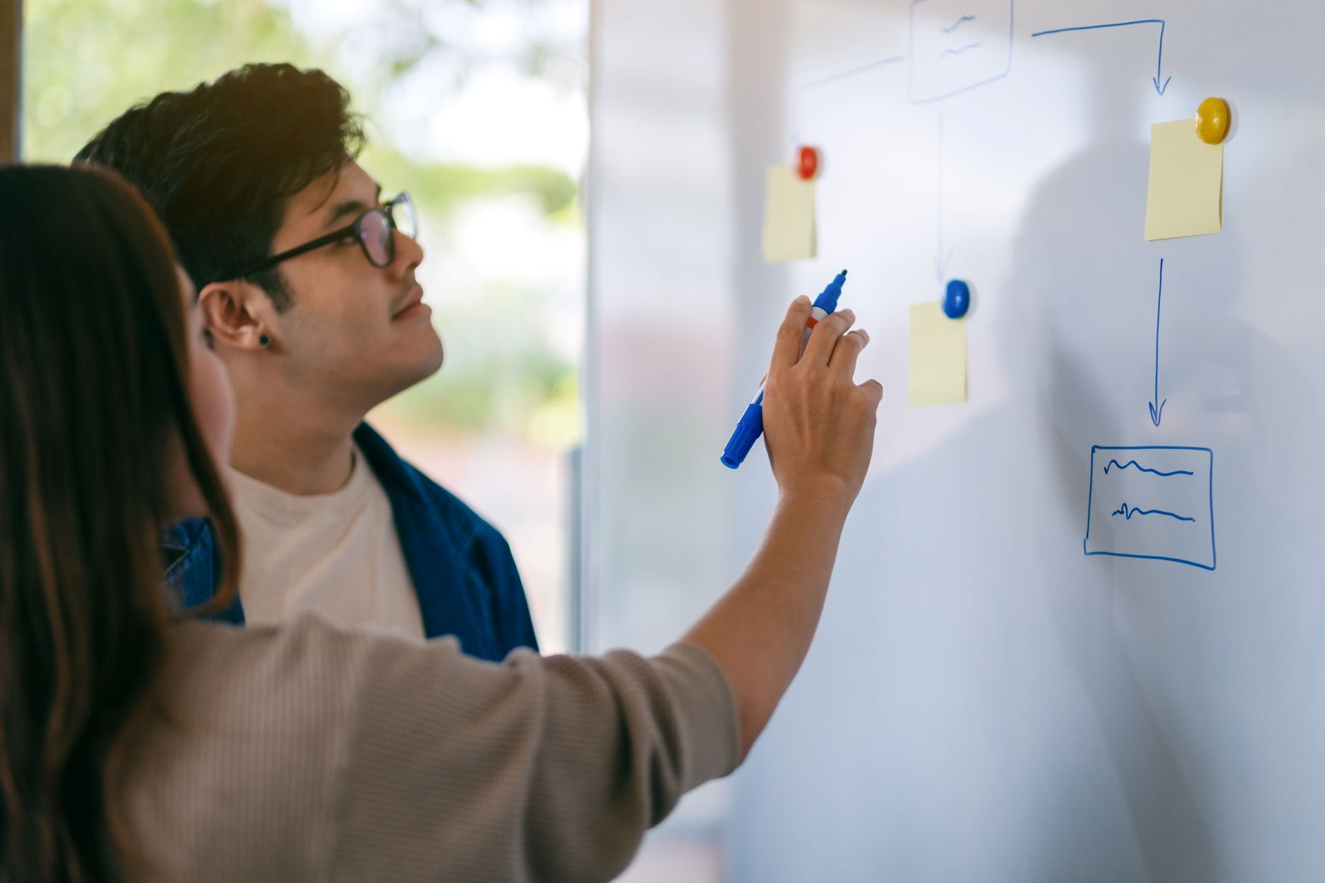 Two team members collaborating at a whiteboard, mapping out a workflow, representing strategic planning and process development.